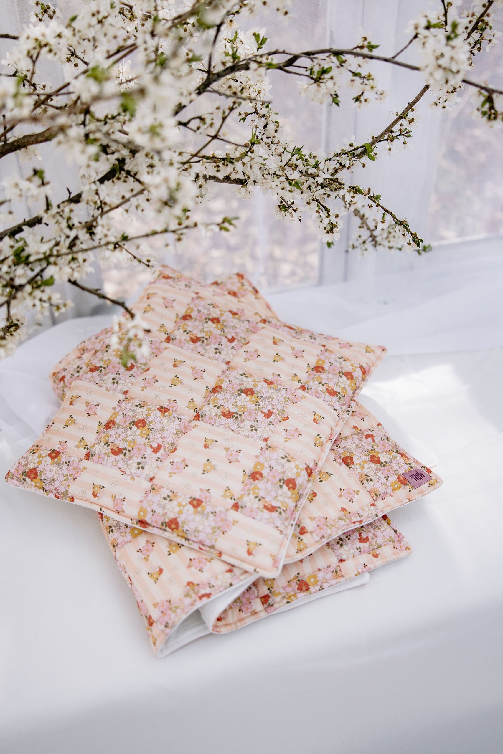 soft cotton quilted patchwork blanket and pillow set in spring garden colors, draped over a cozy nursery chair