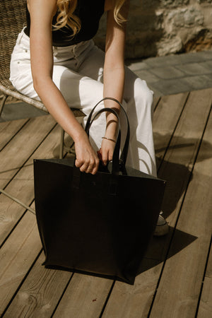 bold black leather bucket bag with structured base and magnetic closure, held confidently by hand
