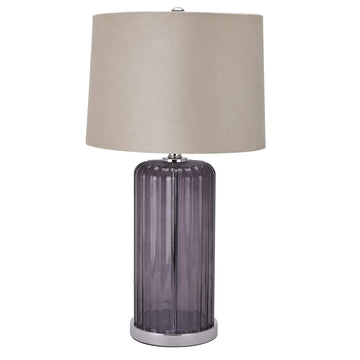 Metallic glass table lamp with fluted texture and beige velvet shade, casting warm ambient light in modern interiors. by Hill Interiors at brixbailey.com