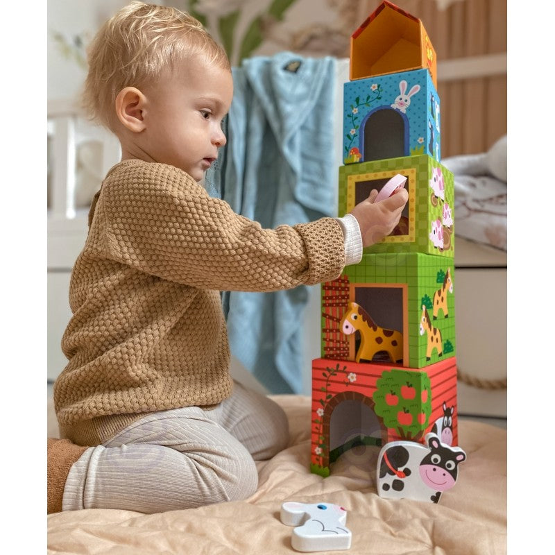 child's hand stacking a green cube with a duck illustration on a sunlit farm puzzle