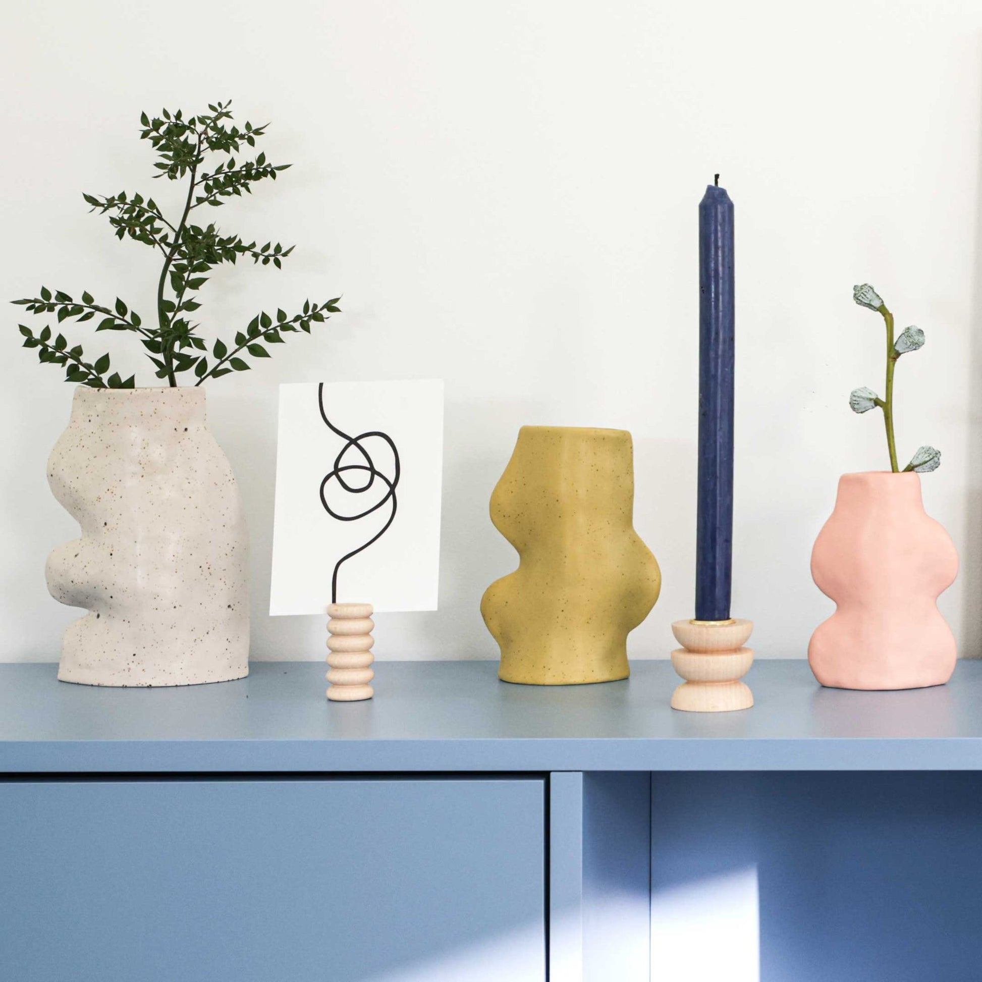 playful pistachio ceramic vase on a sunlit windowsill with a single wildflower