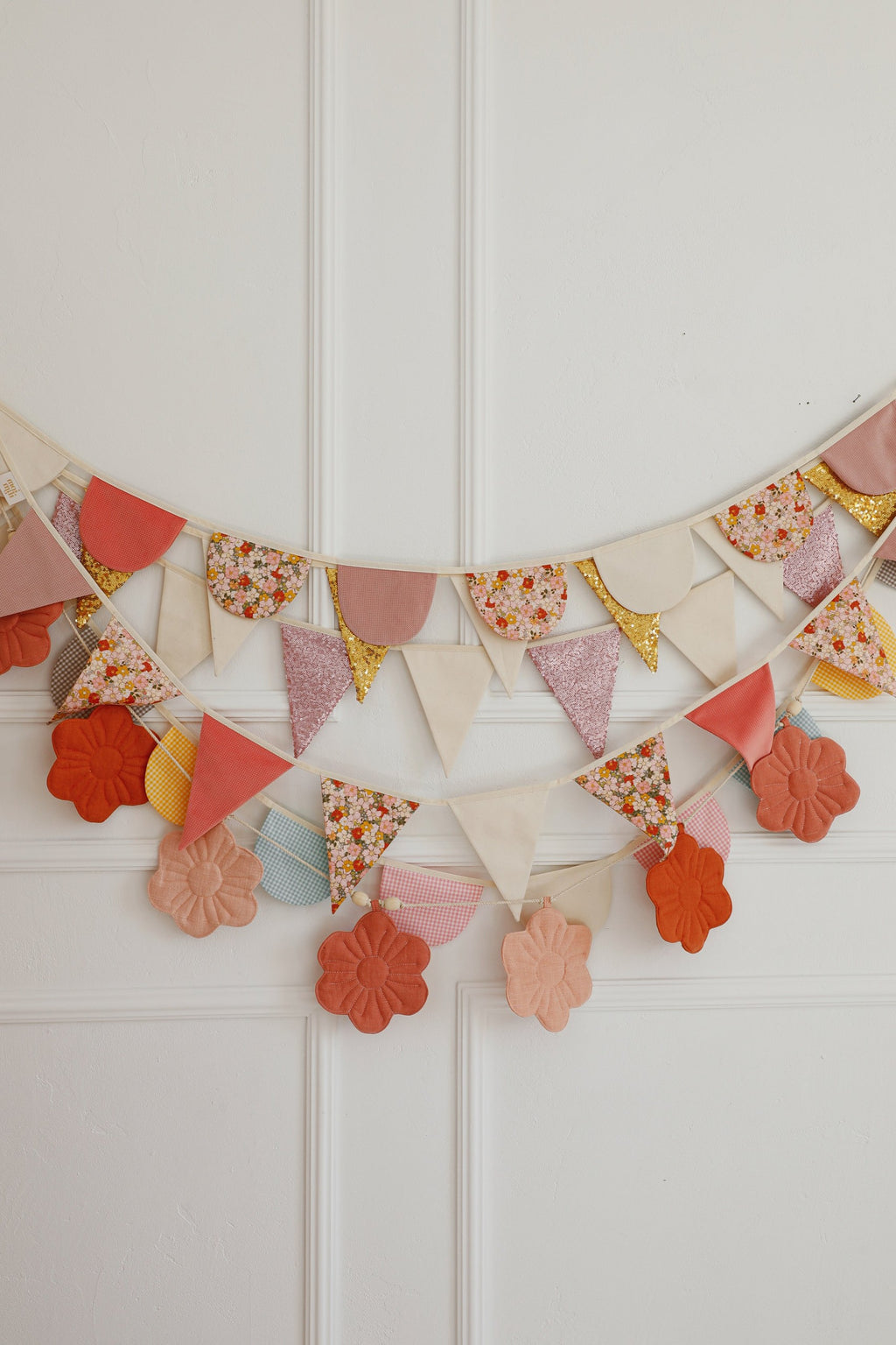 soft pastel birthday garland with cotton and velvet pendants hanging over a sunlit garden-themed nursery