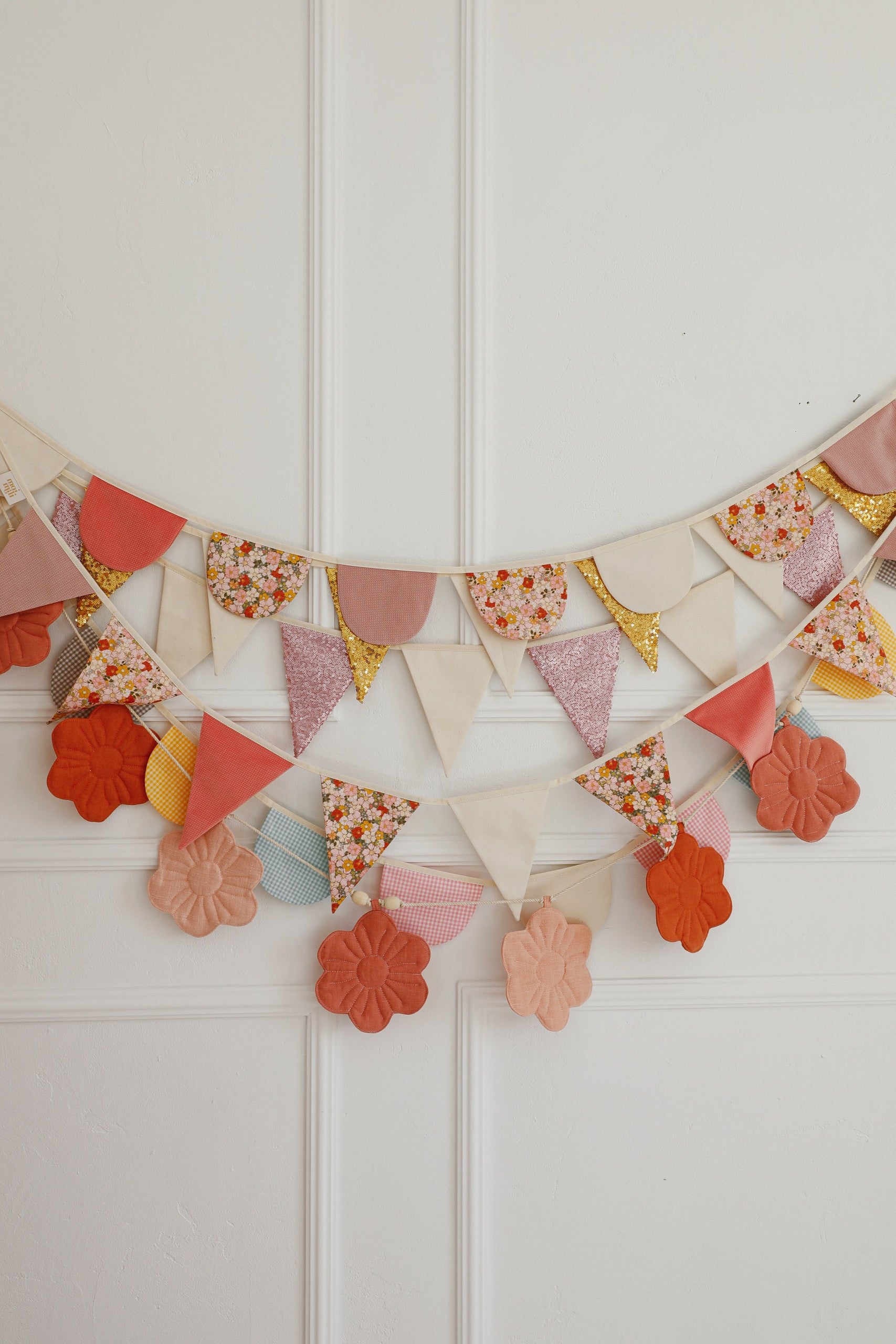 soft pastel birthday garland with cotton and velvet pendants hanging over a sunlit garden-themed nursery