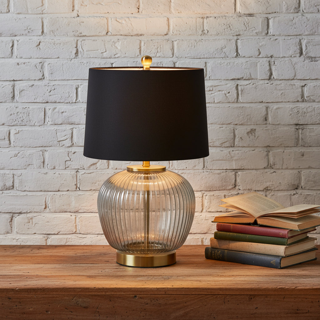 Table lamp with black shade, ribbed glass base, and gold accents on a white background