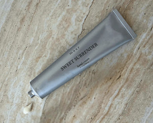 a soft-focus close-up of sweet surrender hand cream being gently squeezed from its tube