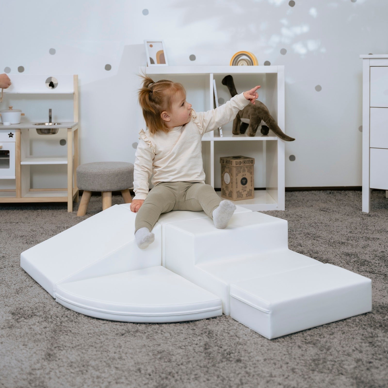 a child's hand reaching for a white foam corner climber block in soft morning light