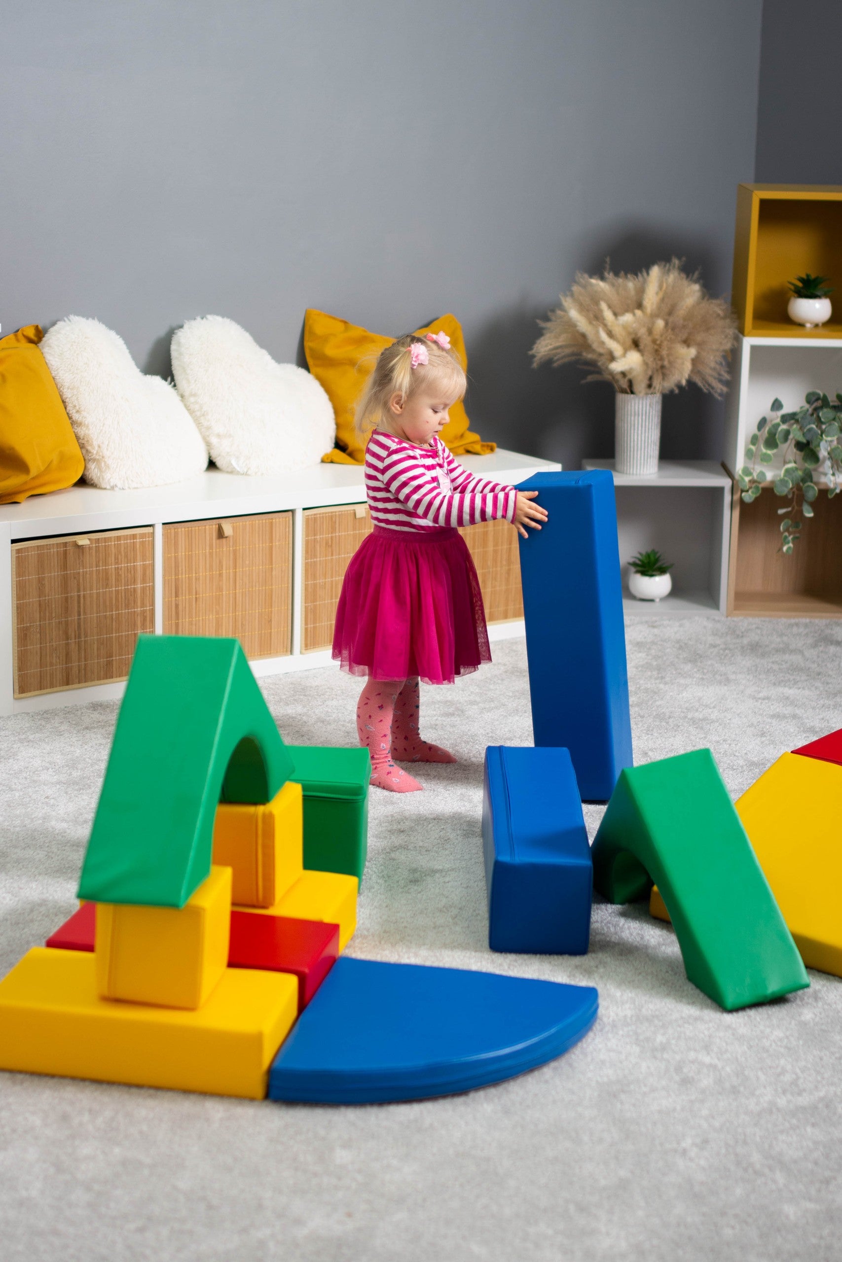 a child's hand placing a soft blue iglu foam block on a colorful tower