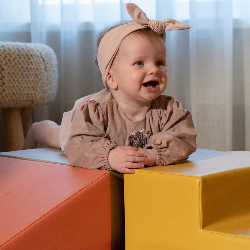 a toddler laughing as they peek from behind a soft pink foam block fort
