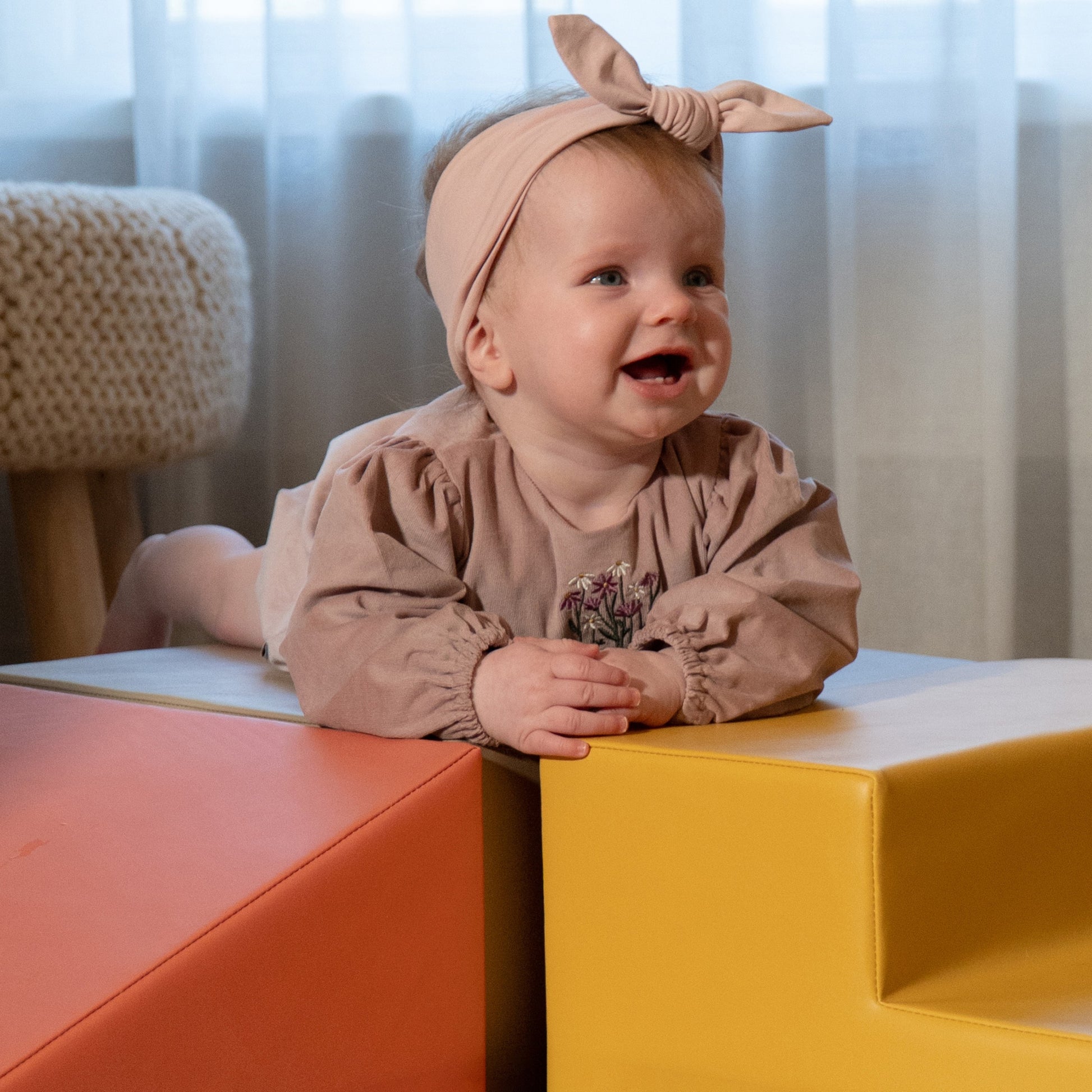 a toddler laughing as they peek from behind a soft pink foam block fort