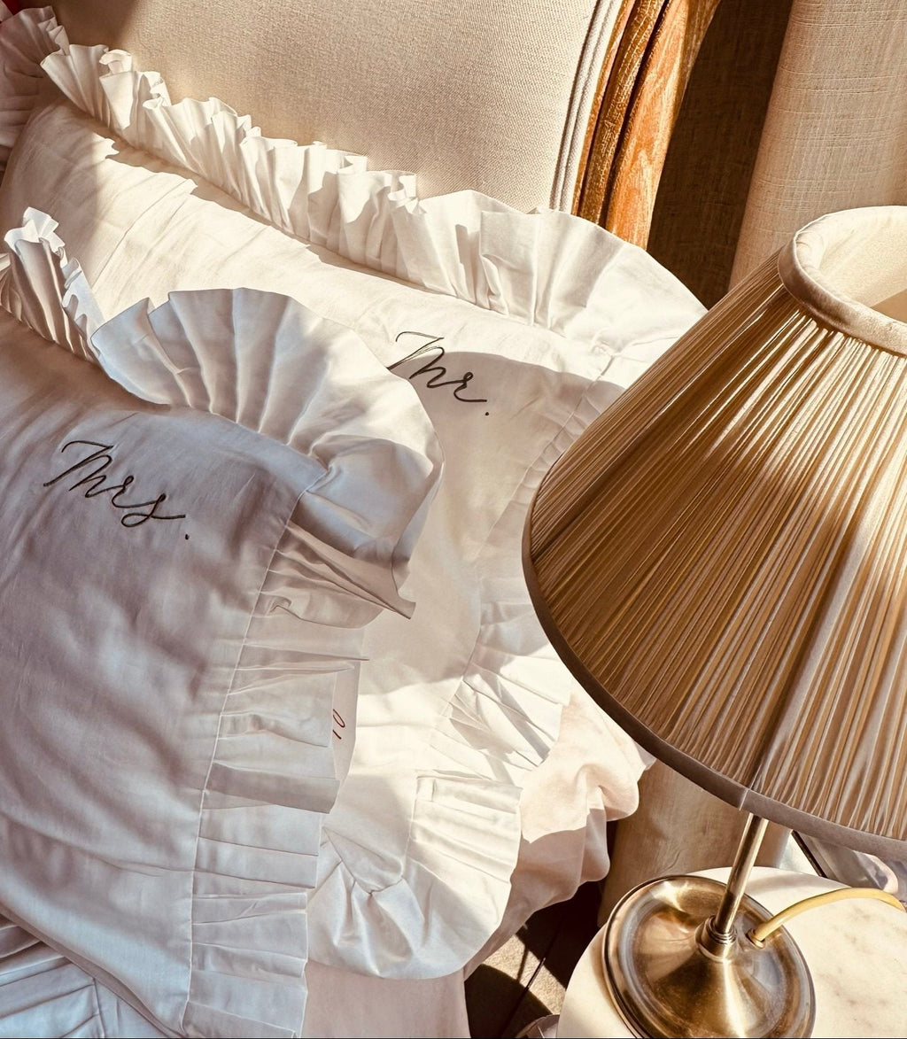 White pillow with 'Mrs.' embroidery on a chair next to a lamp on Sostter.com