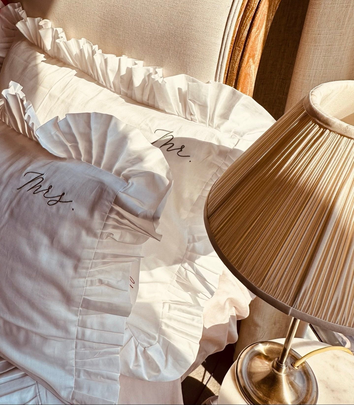 White pillow with 'Mrs.' embroidery on a chair next to a lamp on Sostter.com