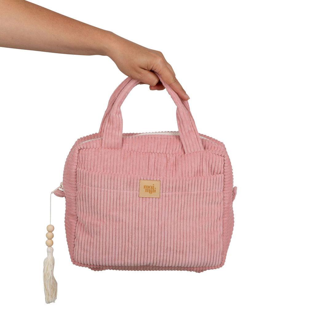 a playful baby pink makeup bag open on a sunlit table with brushes and lipsticks spilling out