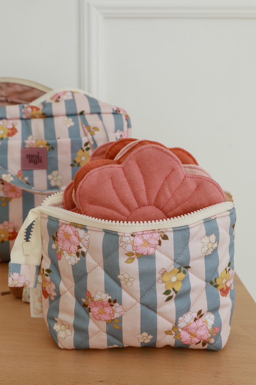 soft blue striped cotton makeup bag with waterproof lining, open to show inner pockets, resting on a cozy linen backdrop