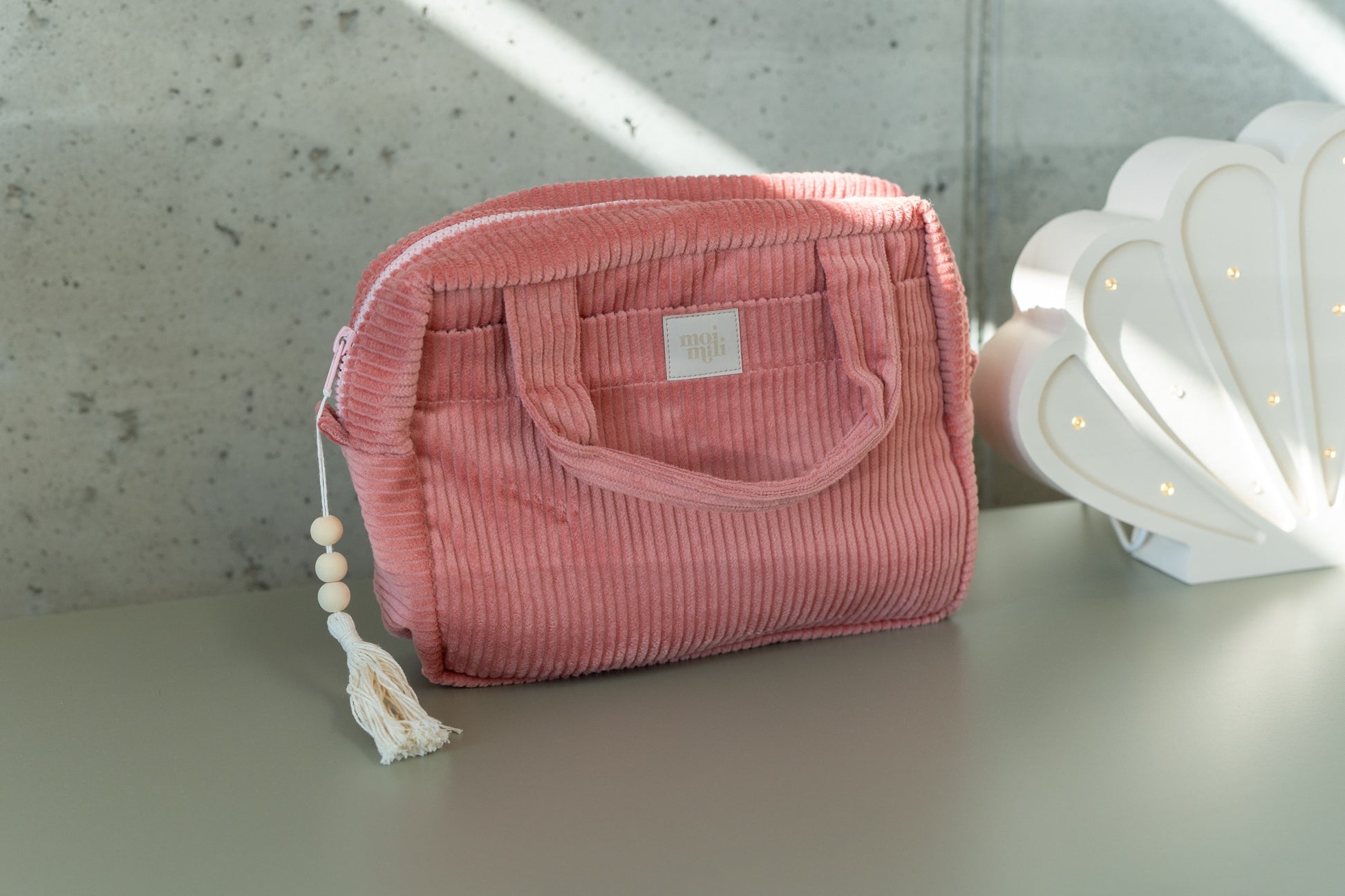 soft coral makeup bag with waterproof lining, open to show inner pockets, resting on a cozy linen backdrop