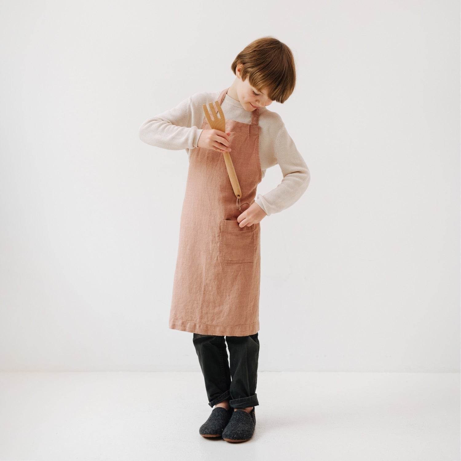 soft cafe creme linen apron for kids with front pocket, tied at waist in cozy kitchen light