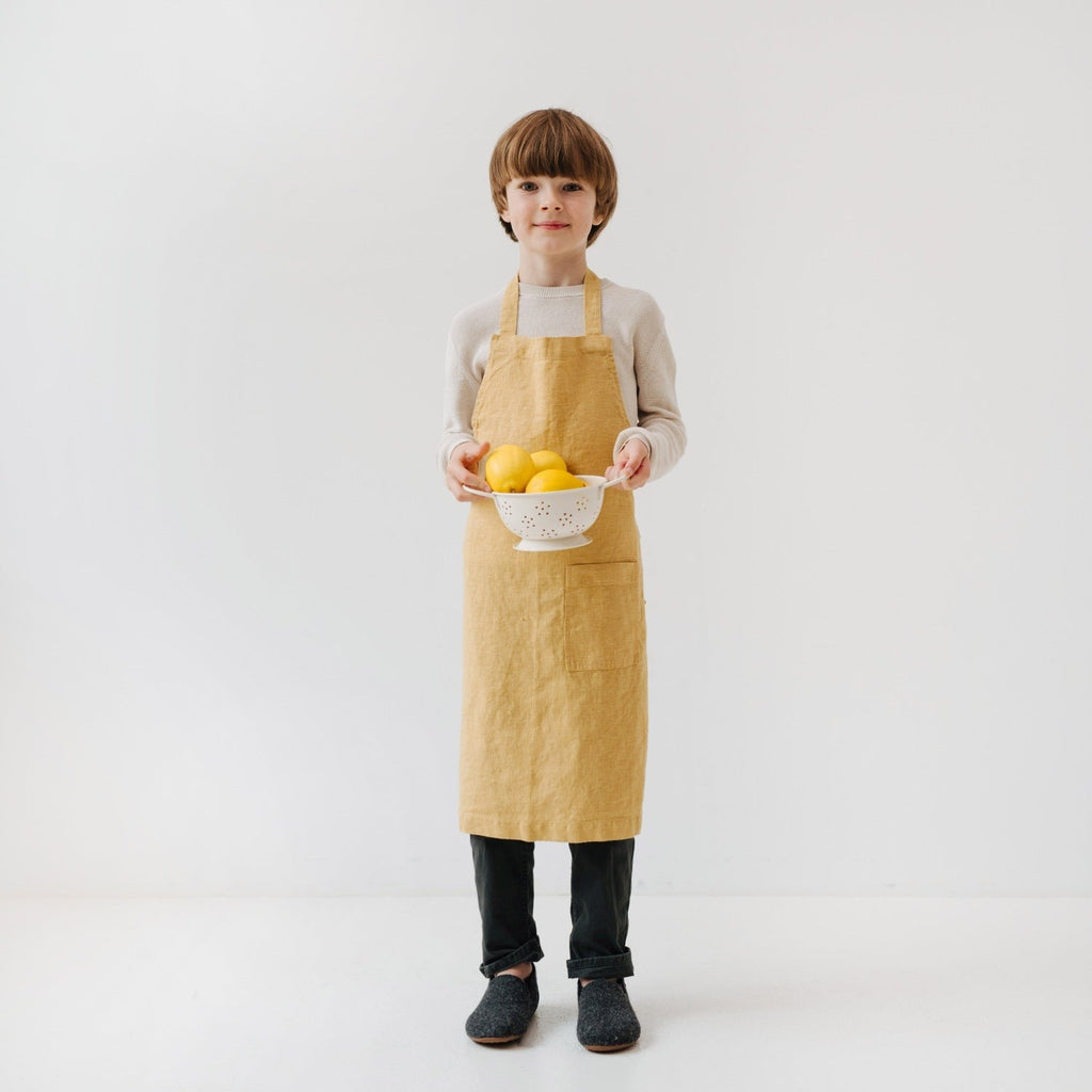 young child in a honey linen apron focused on baking with a wooden spoon