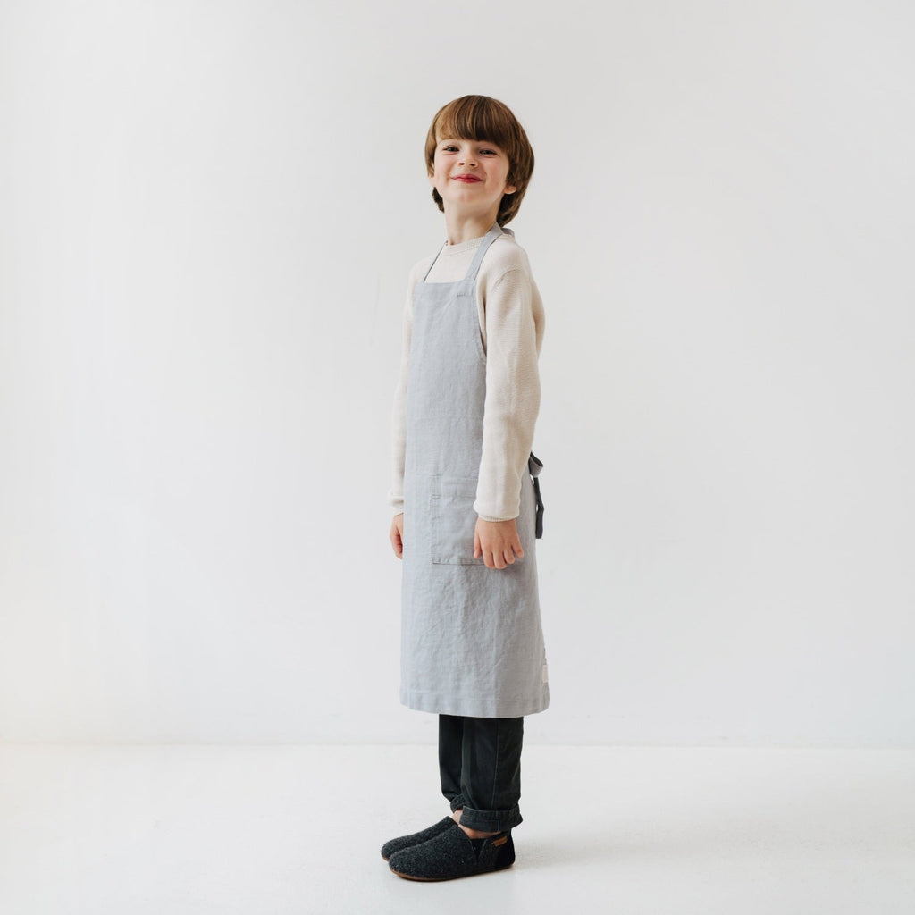 elegant light grey linen kids apron with a front pocket, shown in a refined kitchen setting