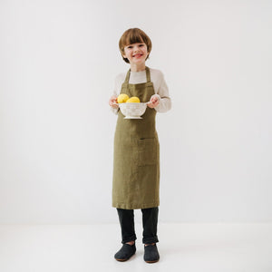 confident young chef in an olive linen apron standing in a sunlit kitchen