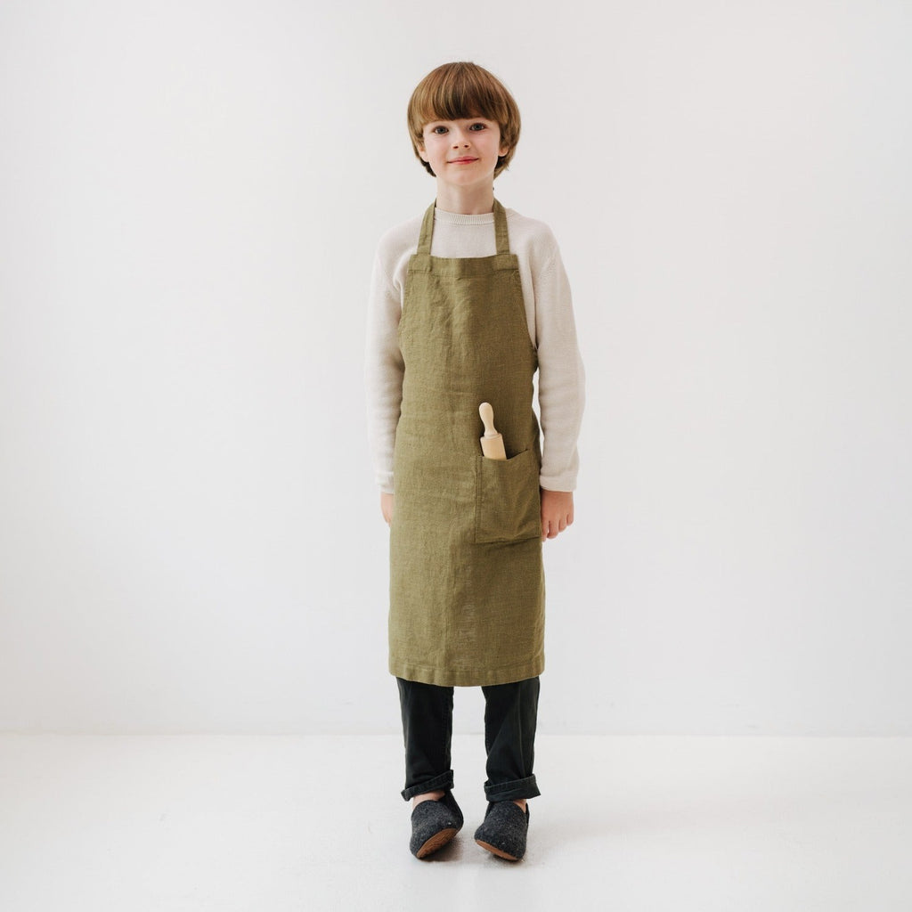 olive linen kids apron with front pocket, tied at waist, ready for kitchen adventures