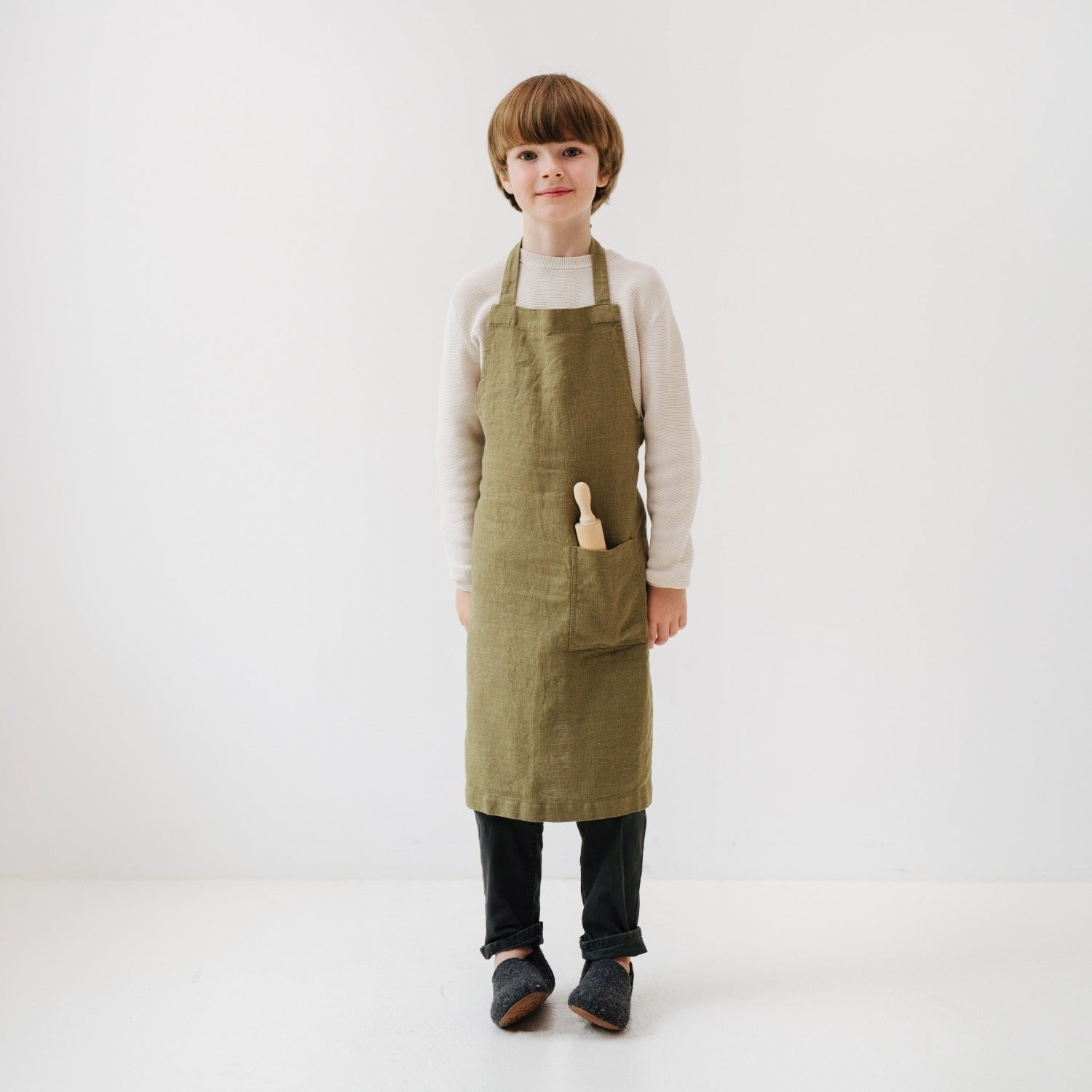 olive linen kids apron with front pocket, tied at waist, ready for kitchen adventures