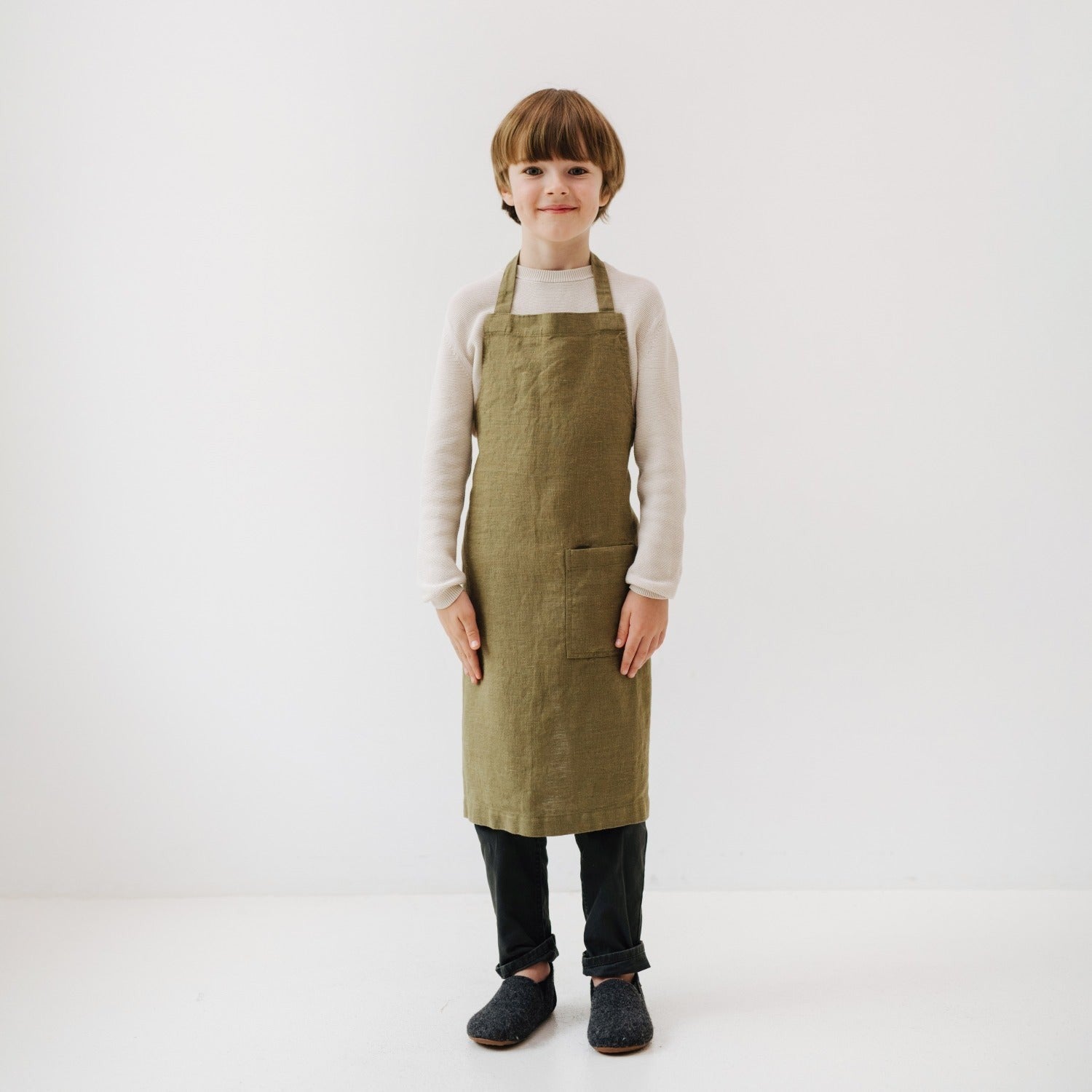 playful olive linen kids apron with front pocket, tied at the waist, ready for kitchen adventures