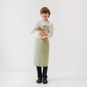 soft sage linen kids apron with a front pocket, shown in gentle natural light
