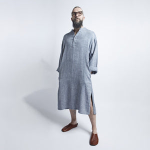 a confident man in a blue gray linen dress standing boldly against an urban backdrop