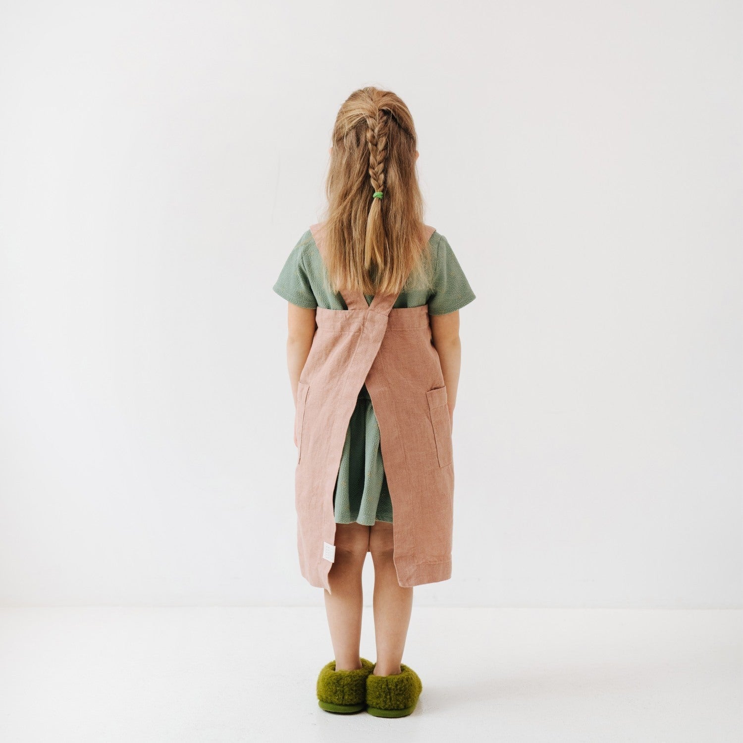 soft honey-colored linen kids apron with pockets, draped gently on a wooden chair in warm sunlight