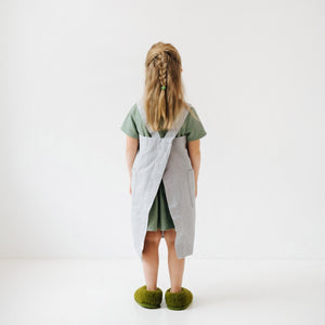 a soft grey linen kids apron with two pockets, shown in gentle morning light