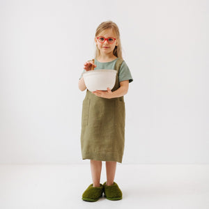 soft olive linen kids apron with two pockets, shown in gentle morning light