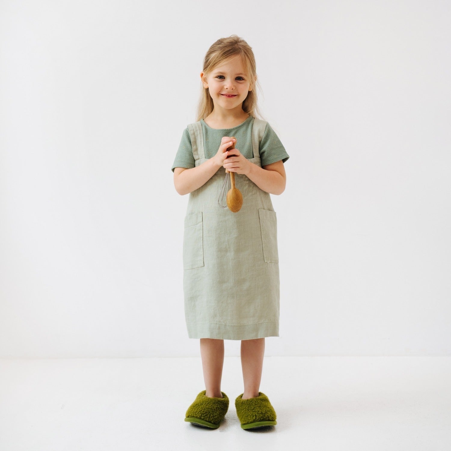 close-up of a child's sage linen apron pockets holding kitchen utensils