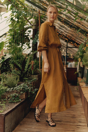 a confident woman in a bronze linen dress with side splits, standing boldly against a sunlit backdrop