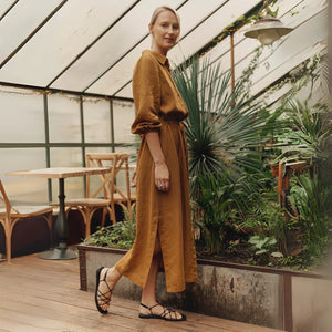 soft bronze linen dress with a relaxed fit and gentle side slits, bathed in warm afternoon light