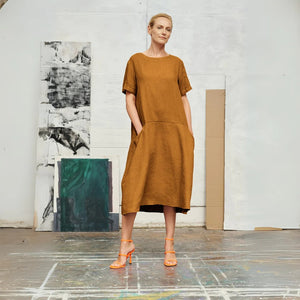 confident woman in a bronze linen a-line dress with front pockets, standing boldly against a minimalist backdrop