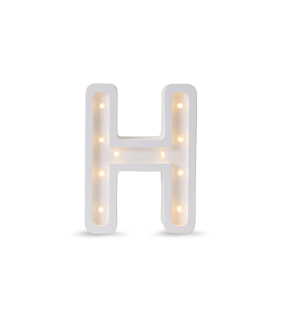 bold solid pinewood letter h lamp glowing warmly on a dark wood surface