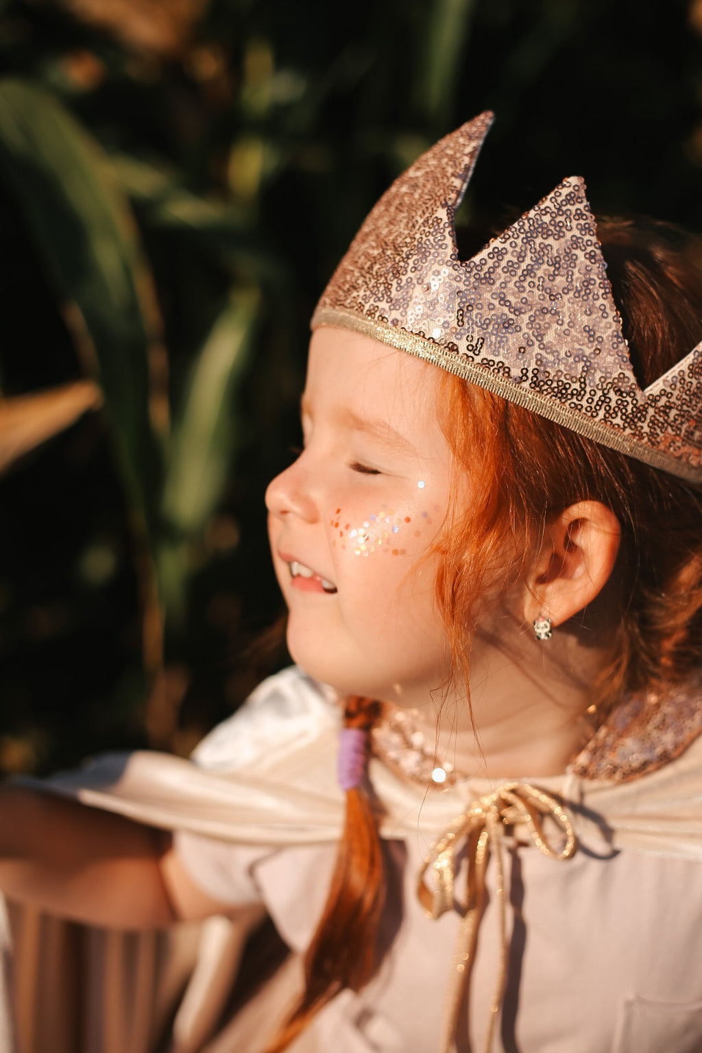 a child laughing, twirling in a cream velour magic cape with a deep hood on a sunny afternoon