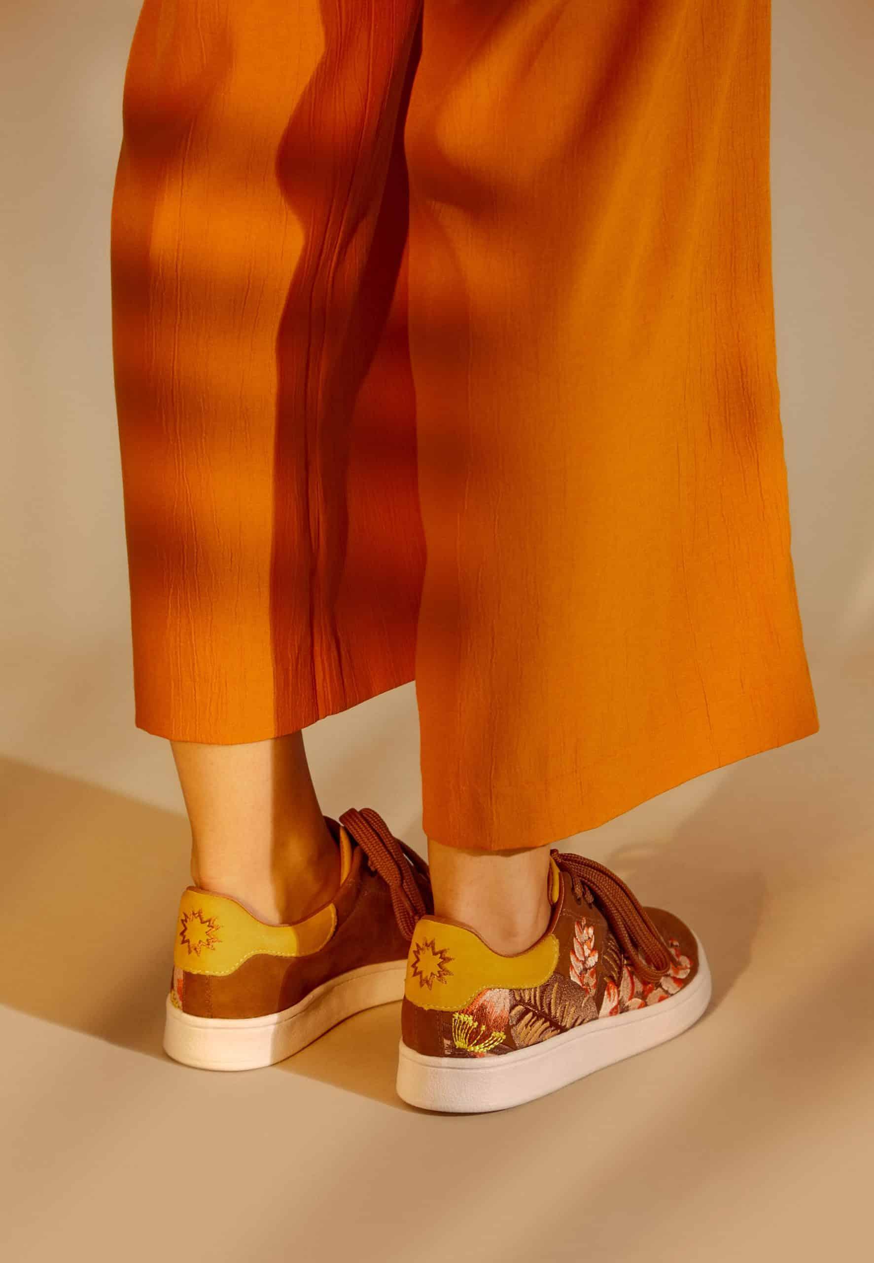 side view of soft brown suede sneakers with intricate floral embroidery on a rustic wooden table