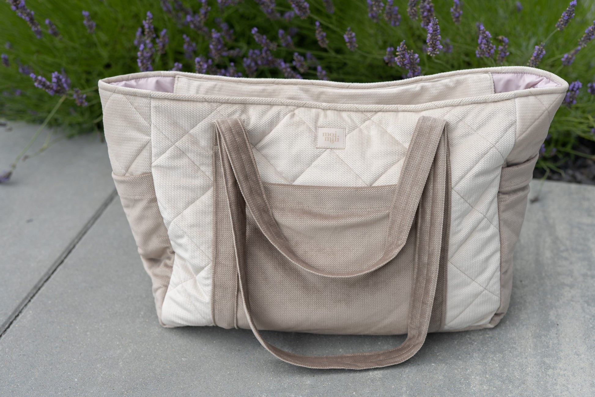 beige velvet weekender bag with dual straps and multiple pockets, laid on a rustic wooden bench