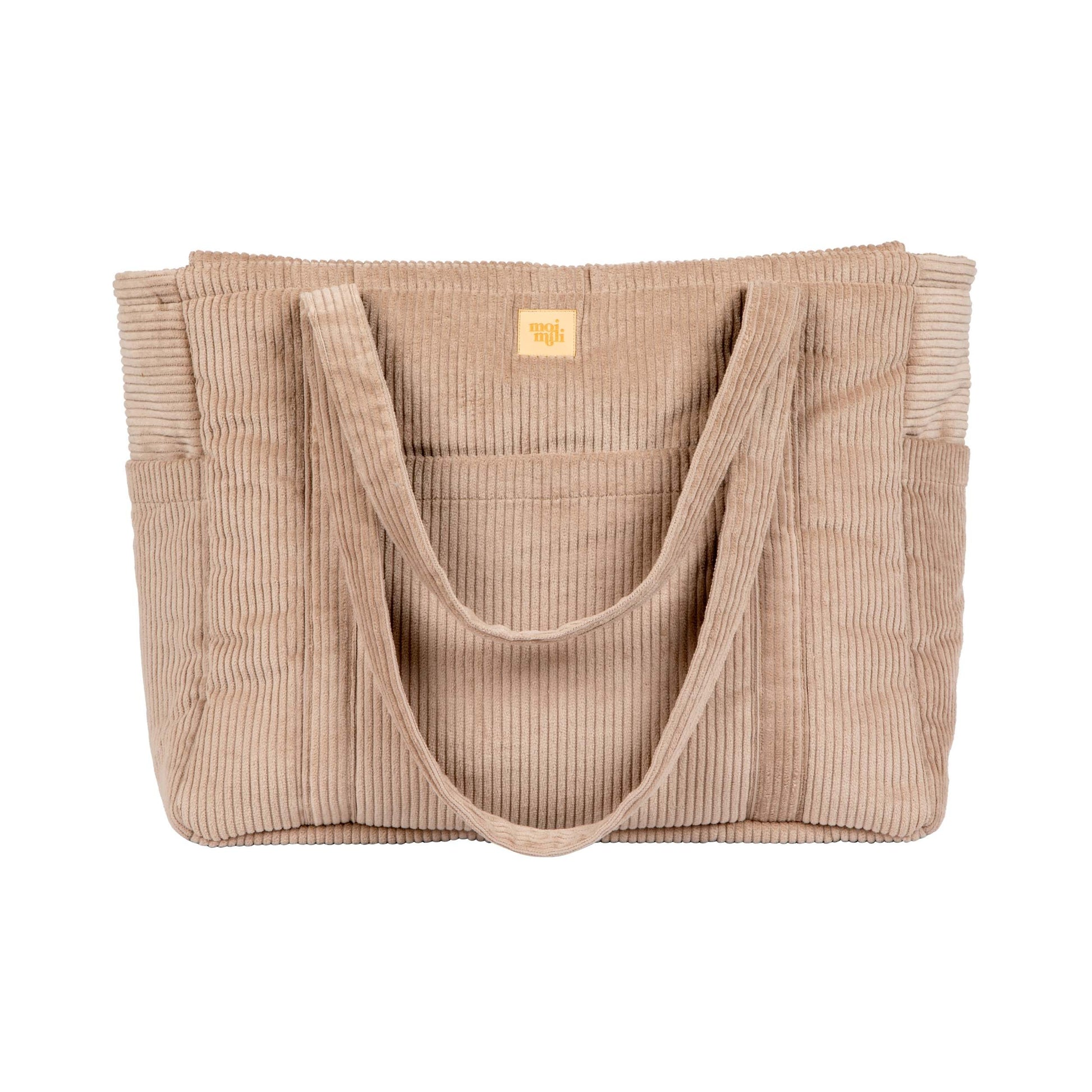 latte-colored velvet weekender bag with dual straps and multiple pockets, resting on a cozy cafe chair