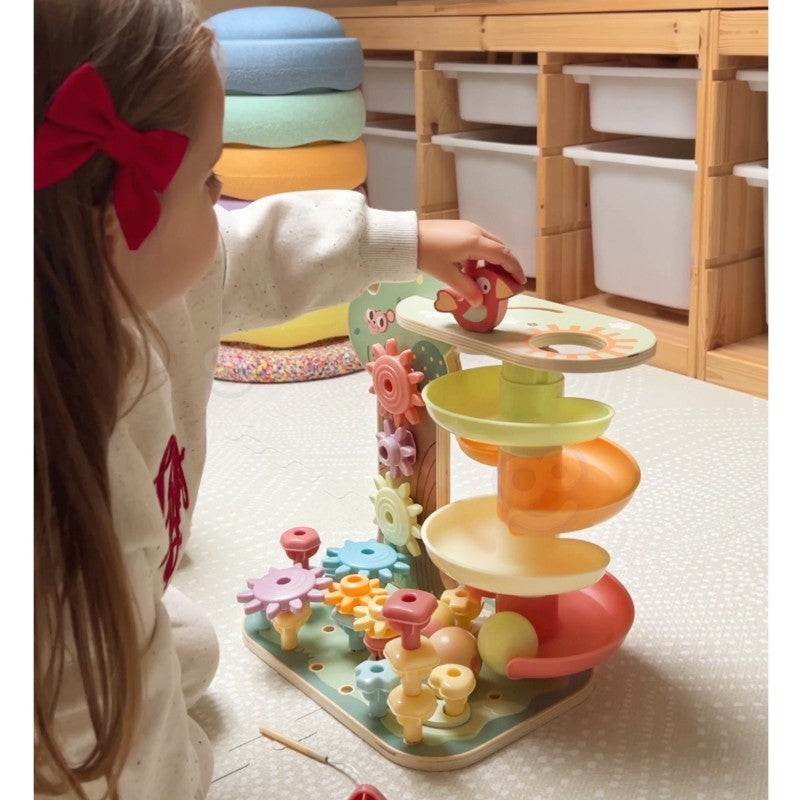 a toddler's hand guiding a wooden ball down the vibrant green track of the montessori activity tree