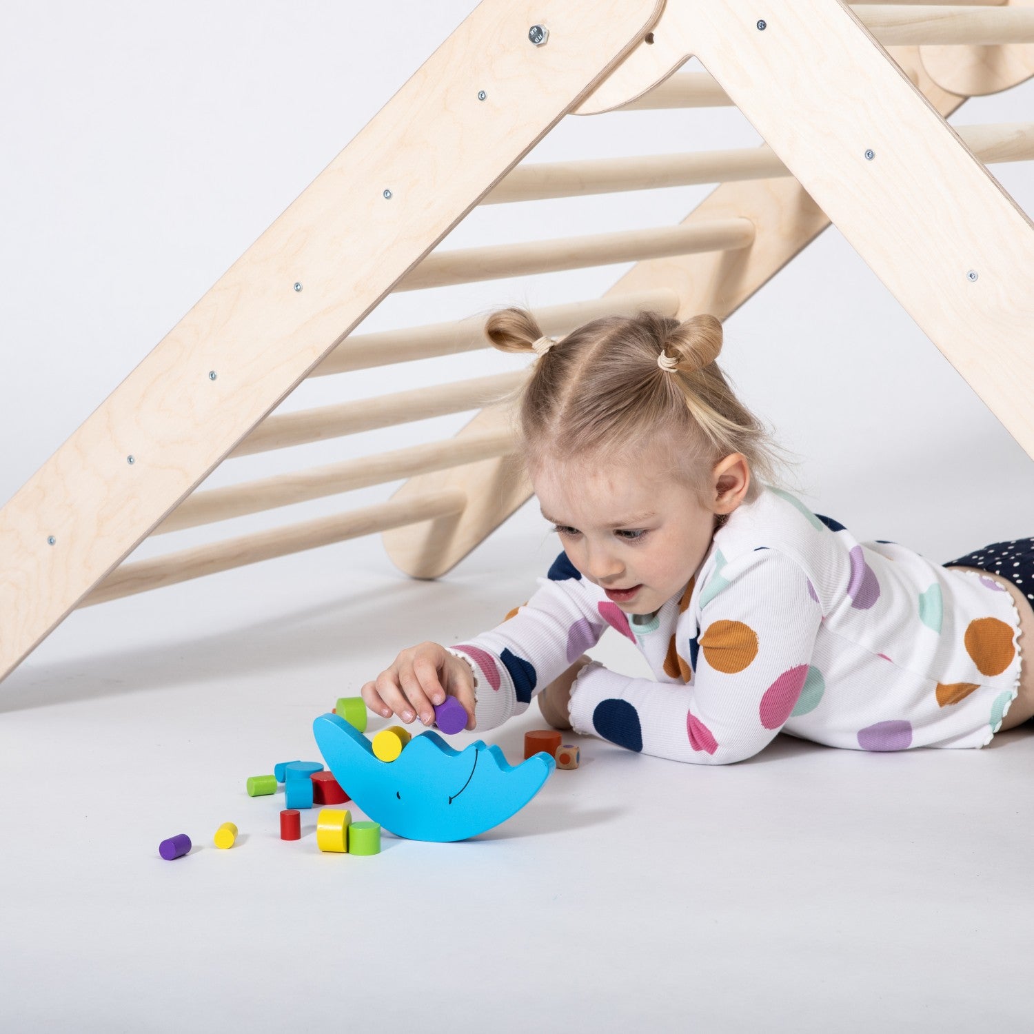 a playful toddler climbing the foldable montessori triangle with bright wooden rings, laughing in a sunlit room