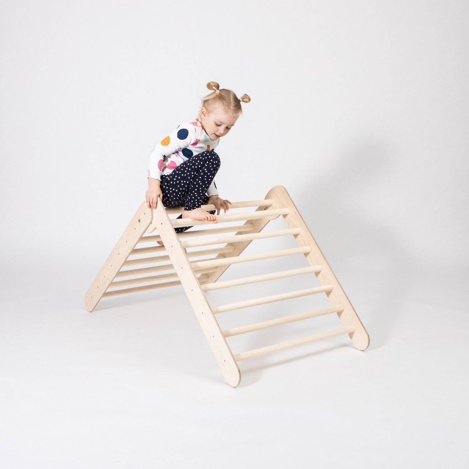 soft-lit montessori climbing triangle with a toddler reaching for the top ring, bathed in warm natural light
