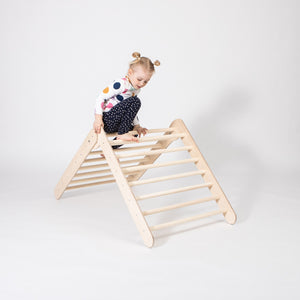 a soft-lit view of a child's hands gently gripping the birch rungs of a montessori climbing triangle