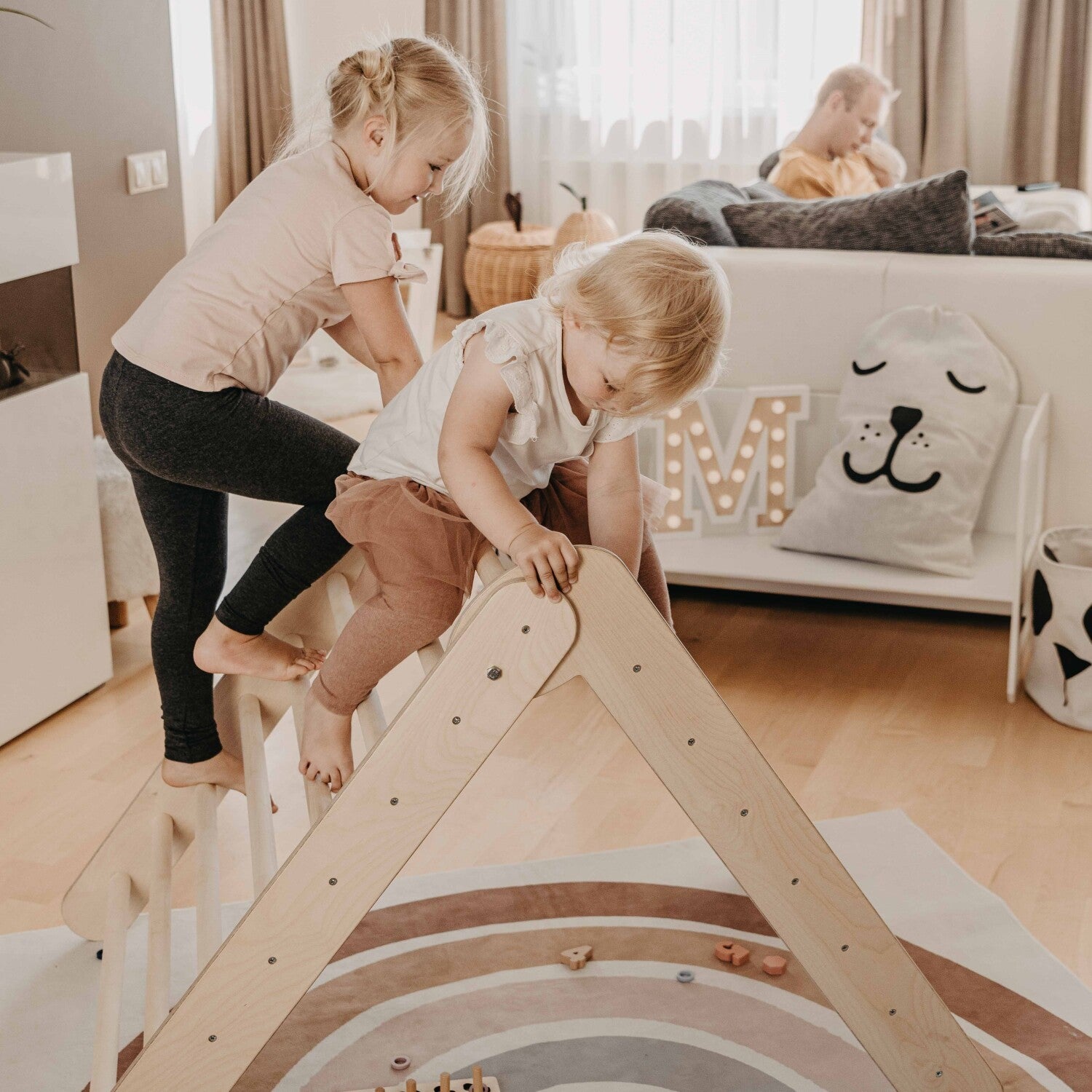 foldable montessori climbing triangle with eight rings per side, shown in a bright room with natural wood tones and a toddler reaching for the top rung