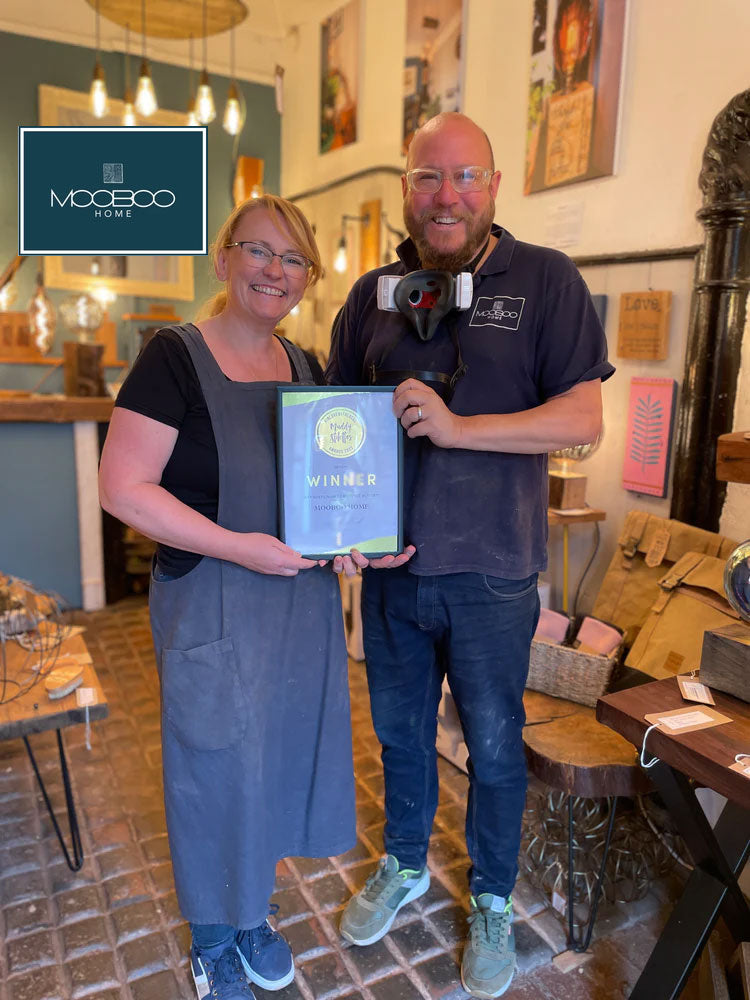 Two people  from indie brand MooBoo Home holding a framed award in a room with decor and furniture on Sostter.com