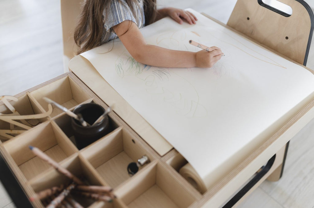 a child's functional art table with open storage boxes and a paper roll ready for creative projects