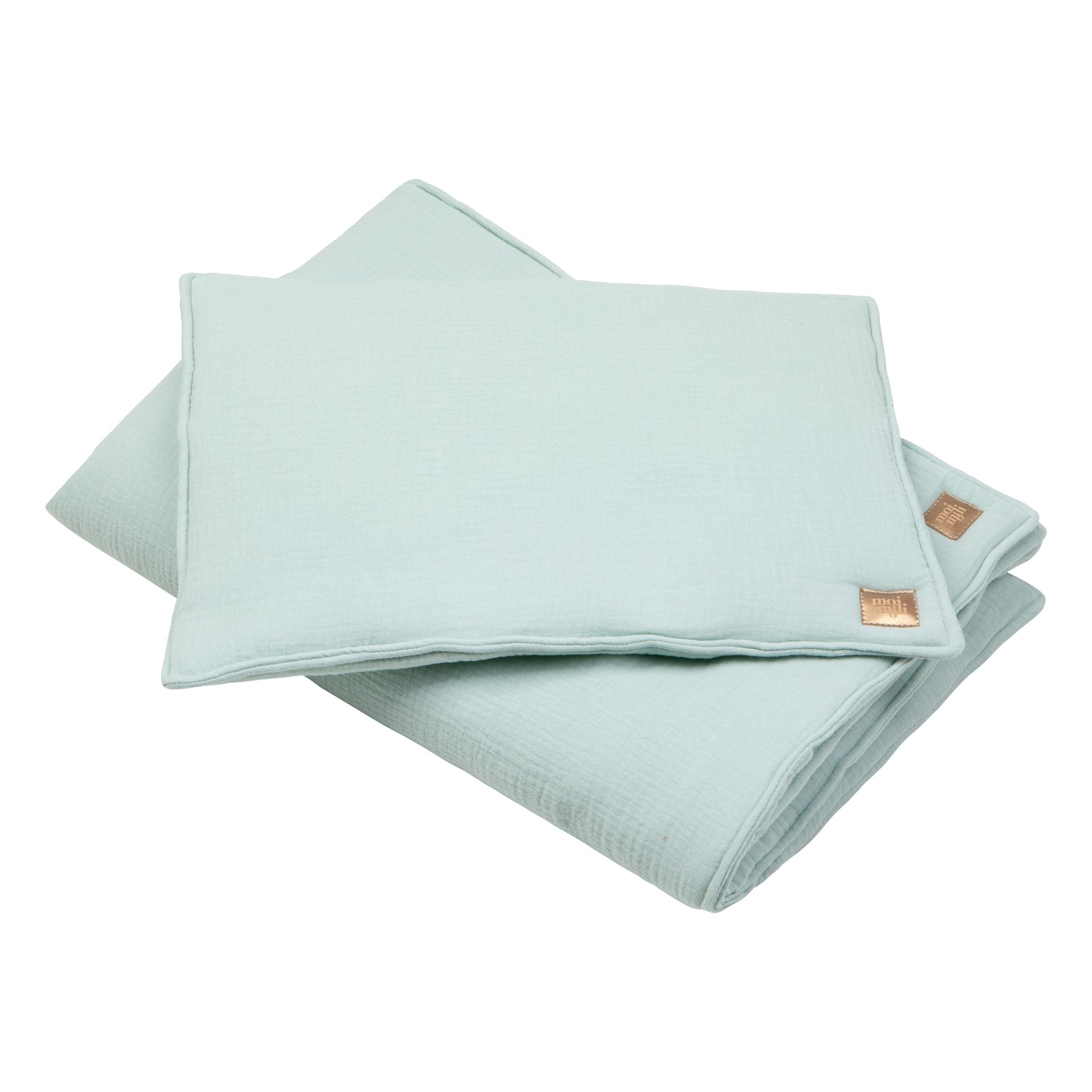 a playful mint muslin baby blanket and pillow set laid out on a sunlit rug