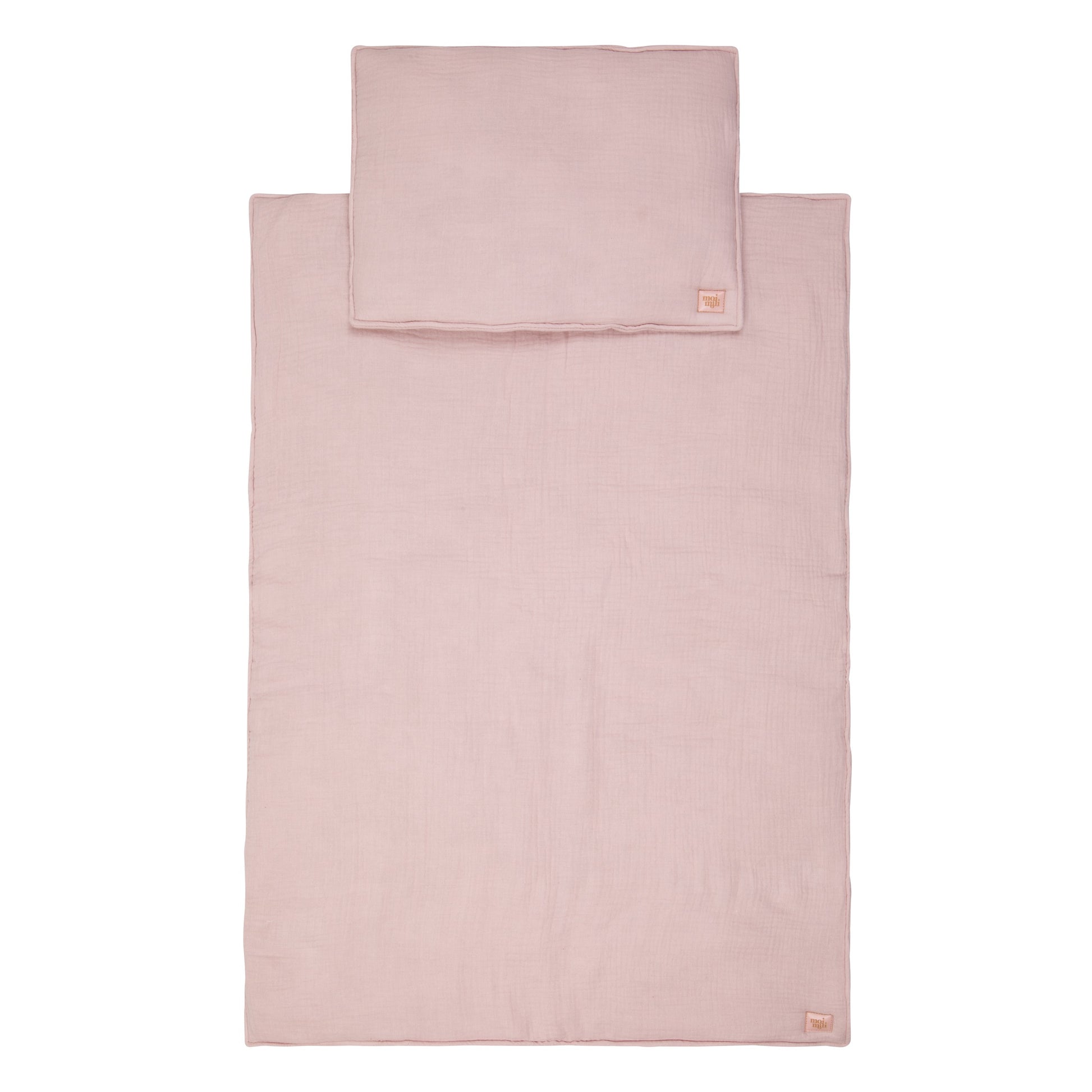 bold baby pink muslin blanket and pillow set laid flat on a rustic wooden table, showcasing soft texture and delicate stitching