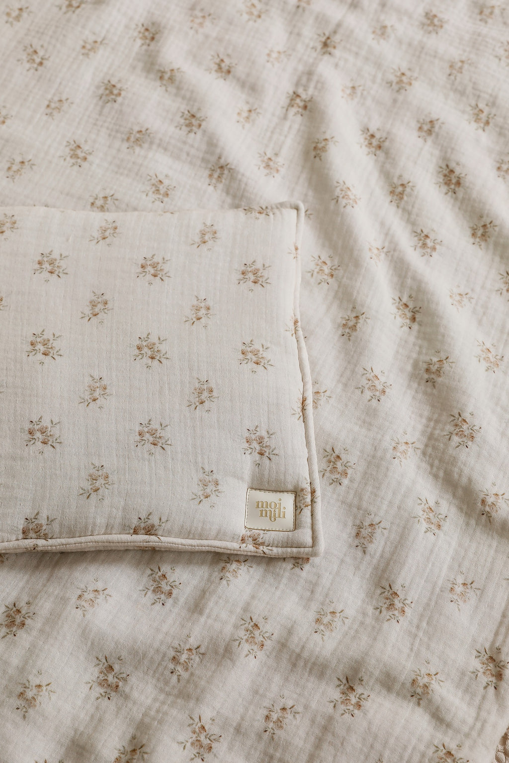 soft boho flower muslin baby blanket and pillow set laid on a rustic wooden cradle, bathed in warm morning light