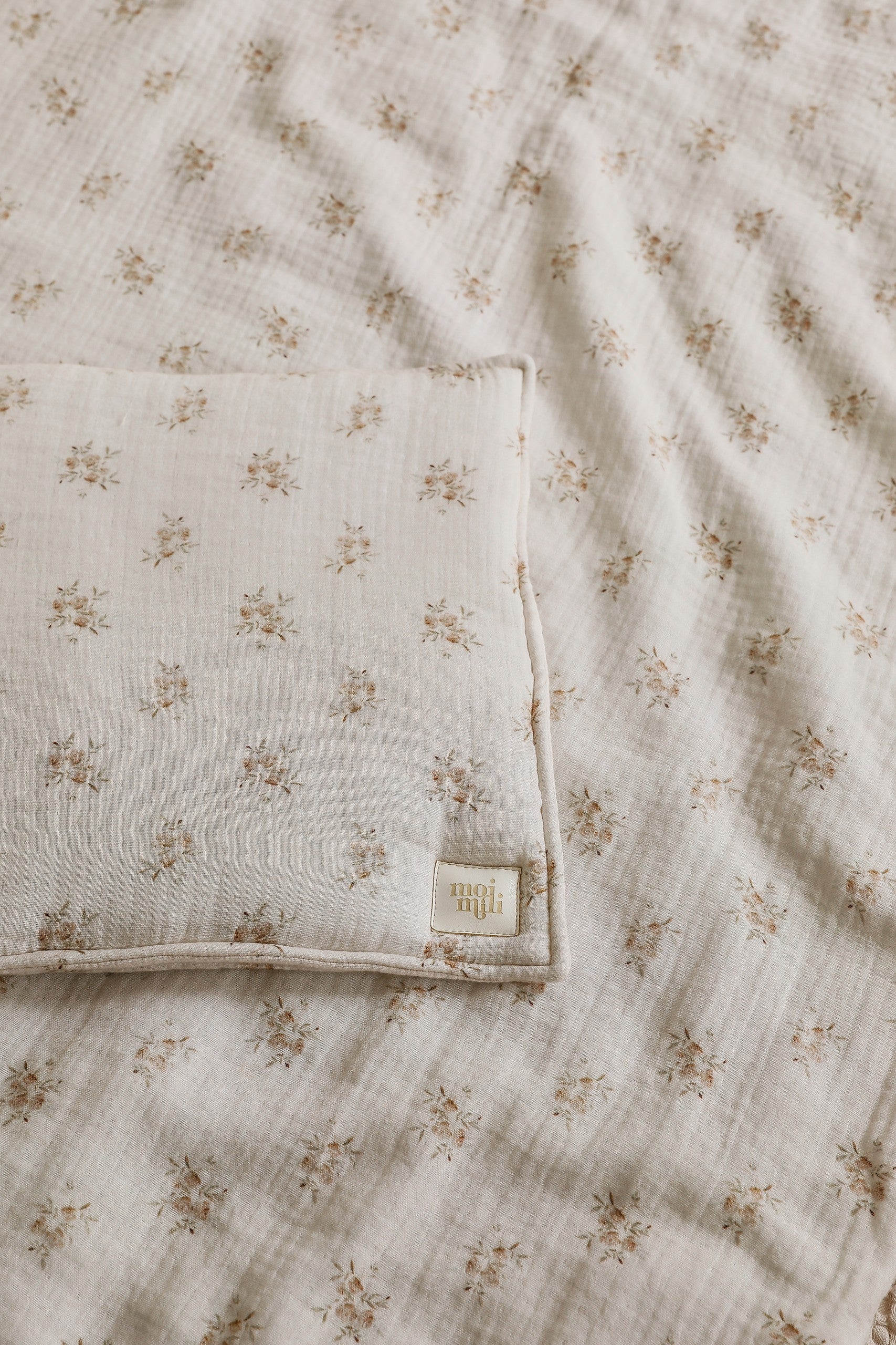 soft boho flower muslin baby blanket and pillow set laid on a rustic wooden cradle, bathed in warm morning light